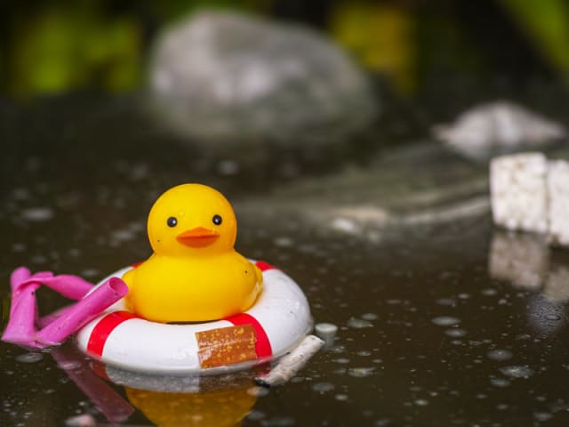 Rubber duck trying to stay afloat among man made trash in the water. Plasticad'A-Mare